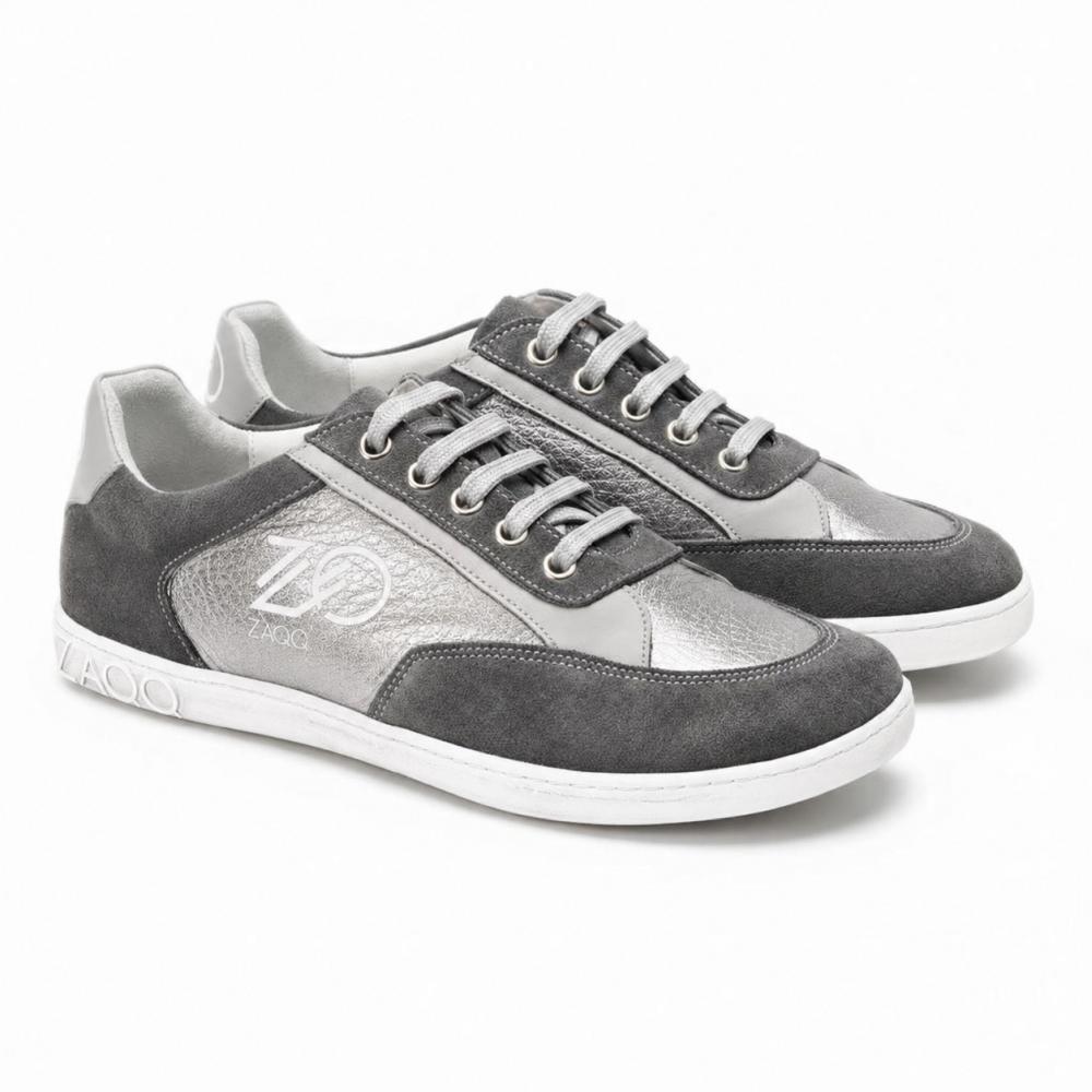Para OQTAV Grey-Sneaker od ZAQQ, wykonane z aksamitnego zamszu i strukturalnych wstawek. Ze srebrnymi sznurówkami i charakterystycznym logo Zagoo z boku i na pięcie, te stylowe buty są prezentowane obok siebie na białym tle.