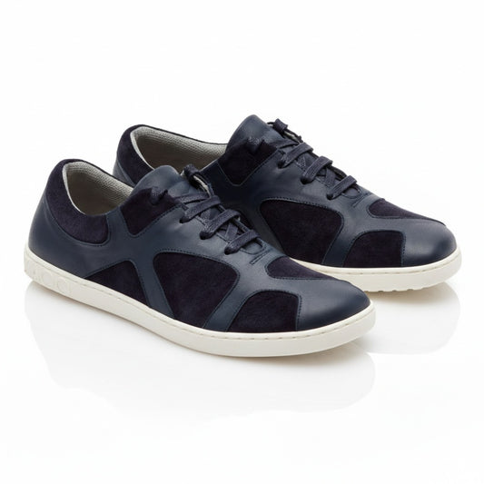 Die QAANAAQ Blue Sneaker von ZAQQ sind aus dunkelblauem Leder und Veloursleder gefertigt, haben weiße Sohlen und einen Schnürverschluss im lässigen Design. Sie bestehen aus atmungsaktivem Material und stehen auf einer weißen reflektierenden Oberfläche.