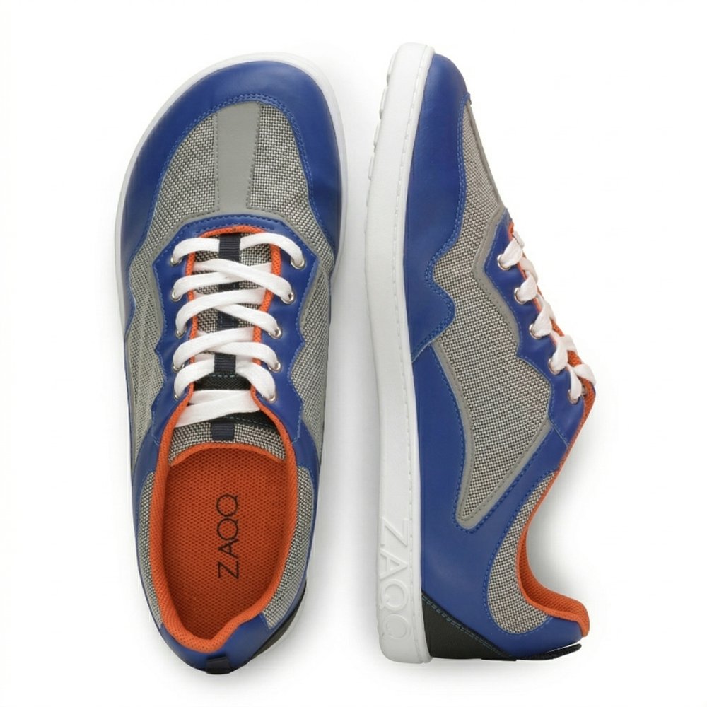 Wir präsentieren die QOPA Blue-Sneaker von ZAQQ, die mit einem breiten Zehenbereich ausgestattet und aus atmungsaktivem Mesh-Gewebe gefertigt sind. Die Seitenansicht des linken Sneakers hebt eine strukturierte weiße Sohle für besseren Halt hervor, während die Draufsicht des rechten Sneakers die Schnürung zeigt und das ZAQQ-Branding deutlich hervorhebt.