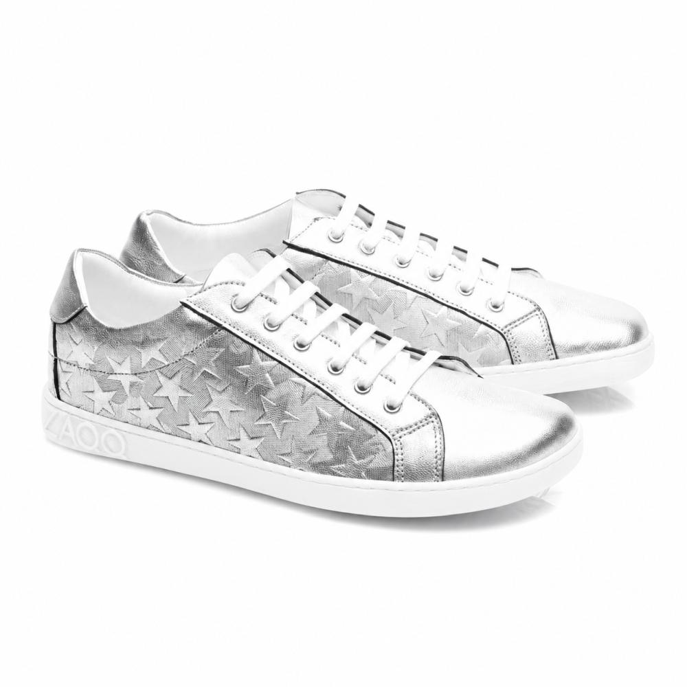 Srebrne trampki SLOQ Stars od ZAQQ mają białe sznurówki i wzór gwiazd po bokach, uzupełnione białą podeszwą z wytłoczonym logo VAOO na pięcie. Te buty wyróżniają się smukłym i nowoczesnym designem z błyszczącym metalicznym wykończeniem.
