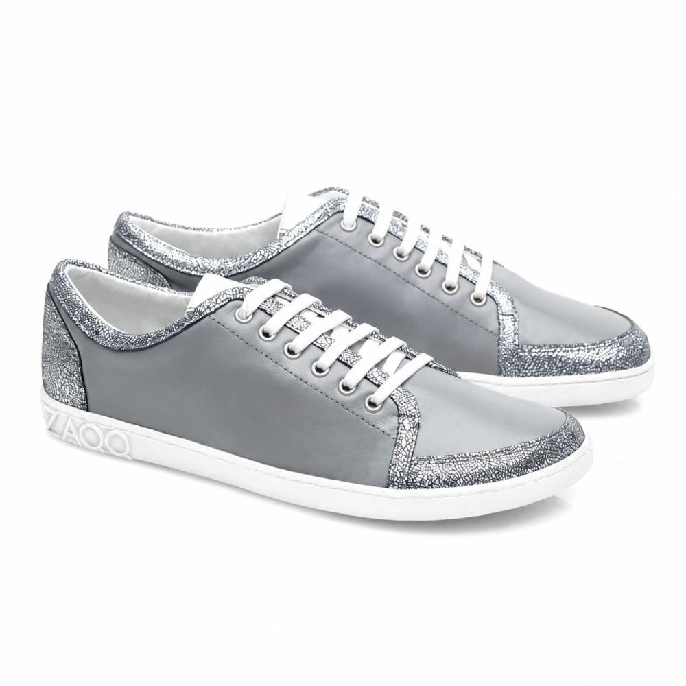 Sneakers TIQQ Grey Silver od ZAQQ zachwycają prostym designem z miękkiej skóry nappa z białymi sznurówkami i srebrnymi, błyszczącymi akcentami, uzupełnionymi przez białe podeszwy i subtelne logo na pięcie, oferując idealne połączenie stylu i komfortu na każdą okazję.